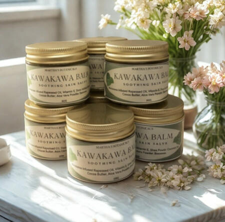 "Stack of Kawakawa Balm jars by Martha's Botanicals surrounded by fresh flowers"
